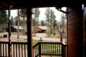 A wooden cabin with a porch, surrounded by trees and a dirt road. - Cozy Woods Cabin Retreat w/ private Hot tub (Lead)