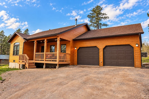 A two-story wooden house with a porch, two garages, and a clear sky.
