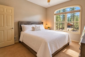 A bedroom with a large bed, a wooden headboard, a window with a view of trees, and a door.