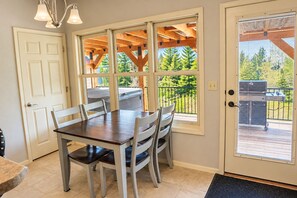 A dining area with a table and chairs, large windows, and a view of a deck and trees.