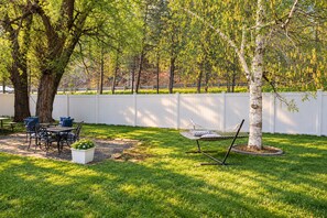 Ein Garten mit Esstisch, Stühlen, einer Hängematte und einem weißen Zaun.