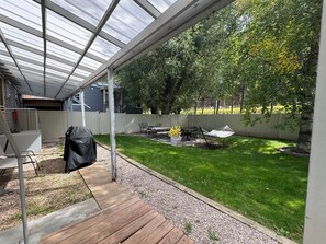 Un patio techado con terraza de madera, una parrilla y mobiliario exterior.