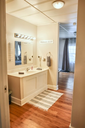 A bathroom with a vanity, a mirror, a towel rack, and a sign reading 'POWDER ROOM'.