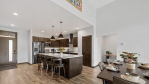 A modern kitchen with a central island, bar stools, and a dining area with a table set for two.