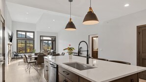 A modern kitchen with a large island, pendant lighting, and a view of the outdoors.