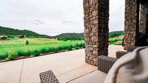 Un pilier de pierre, une terrasse en béton et une vue sur un champ verdoyant avec des maisons au loin.