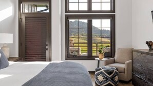 Une chambre avec un grand lit, une porte en bois et une vue sur un paysage verdoyant par la fenêtre.
