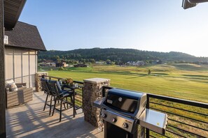 Une terrasse avec un barbecue et des meubles d’extérieur, offrant une vue sur un terrain de golf et un quartier résidentiel.