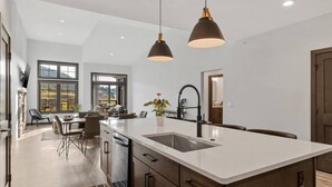 Une cuisine moderne dotée d’un grand îlot central, de luminaires suspendus et offrant une vue sur l’extérieur.