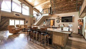 Un vaste espace de vie doté d’un grand plafond en bois, d’un bar avec des tabourets, d’une cheminée et d’un escalier menant à un niveau supérieur.