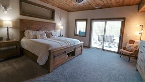 Une chambre à coucher avec un lit en bois, deux lampes de chevet, un ventilateur de plafond et une vue sur l’extérieur grâce à une porte-fenêtre coulissante.