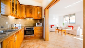A kitchen with wooden cabinets, a microwave, and a stove. There is a dining area with a white sofa and a coffee table. - Villa Alte Springs (Loulé)