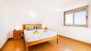 A bedroom with a wooden bed, two bedside tables, a nightstand, and a window with a view. - Villa Alte Springs (Loulé)