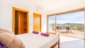 A bedroom with a bed, two pillows, a view of a balcony with outdoor furniture, and a wooden door. - Villa Alte Springs (Loulé)