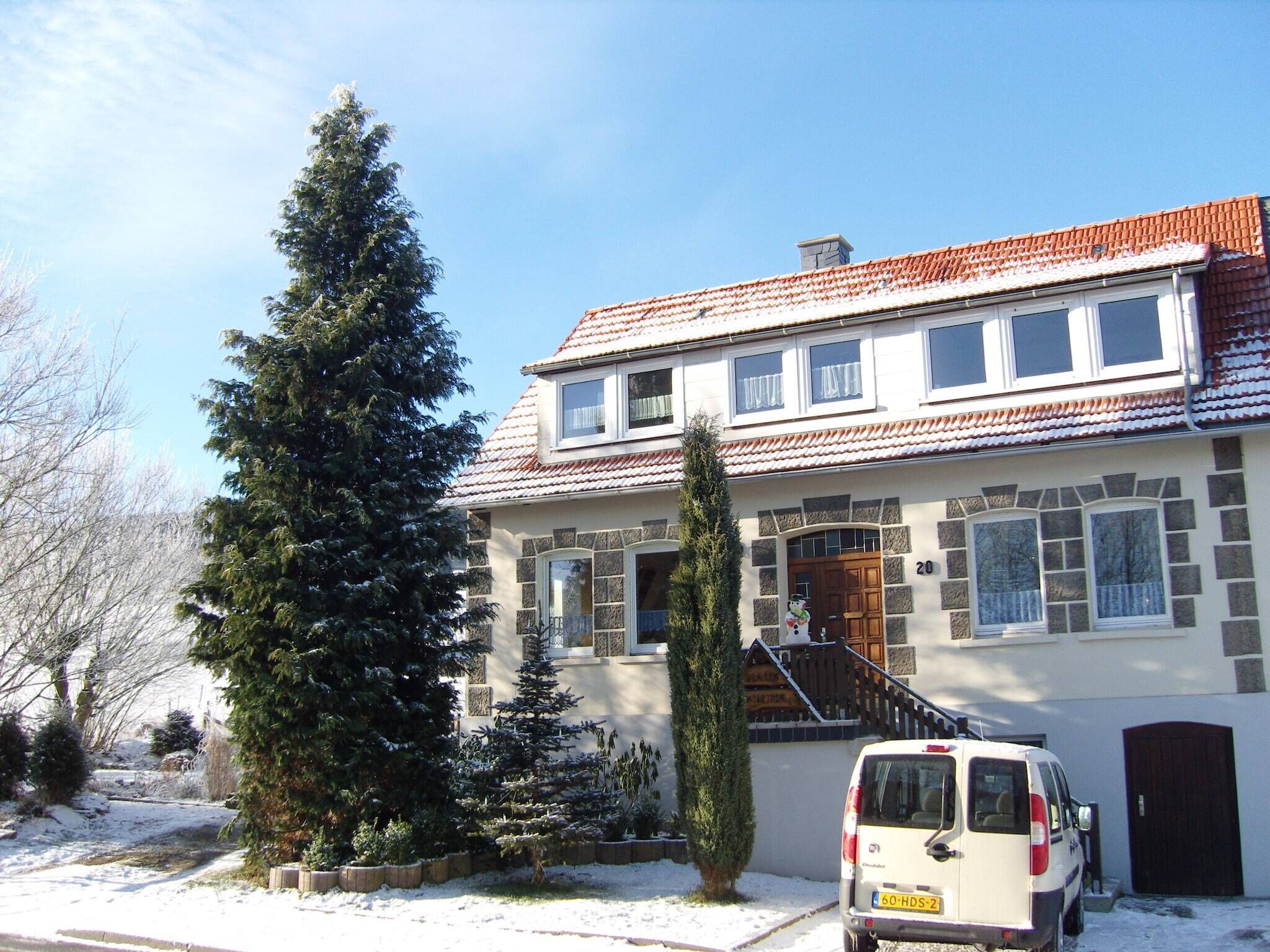 A two-story house with a tiled roof, a front door, and a vehicle parked in the driveway.