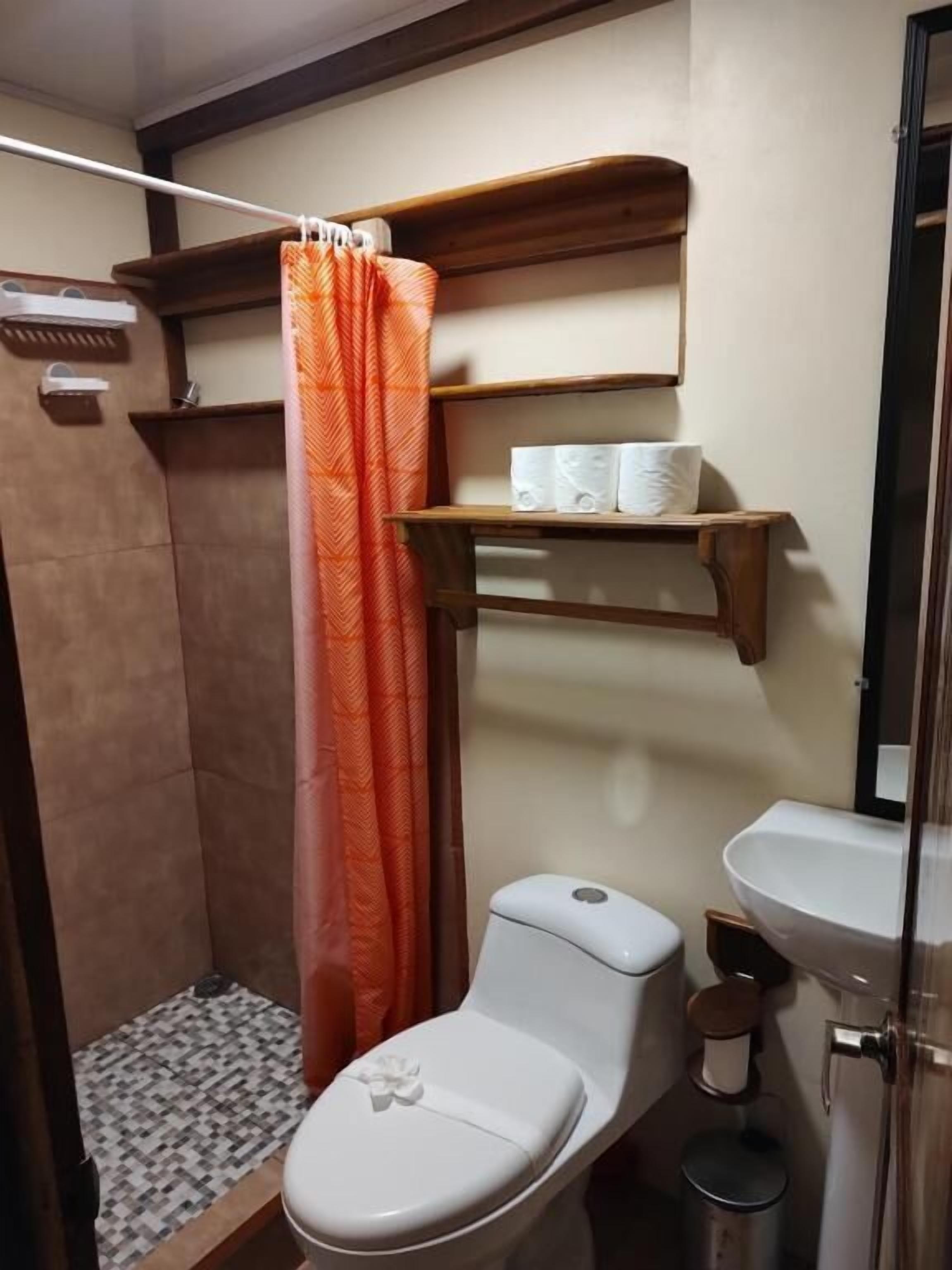 A bathroom with a shower, toilet, sink, and storage shelves.