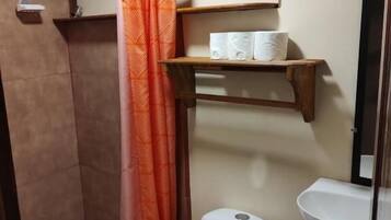 A bathroom with a shower, toilet, sink, and storage shelves.