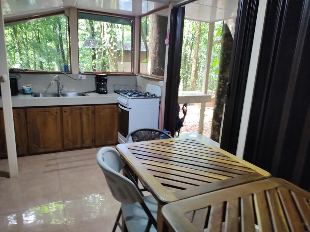 A kitchen with a sink, stove, and dining area with chairs.