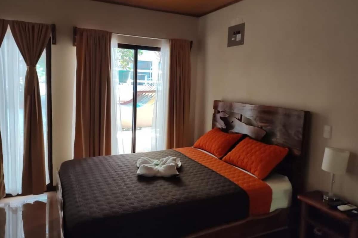 Une chambre d’hôtel avec un lit, des rideaux, une fenêtre et une table de chevet.