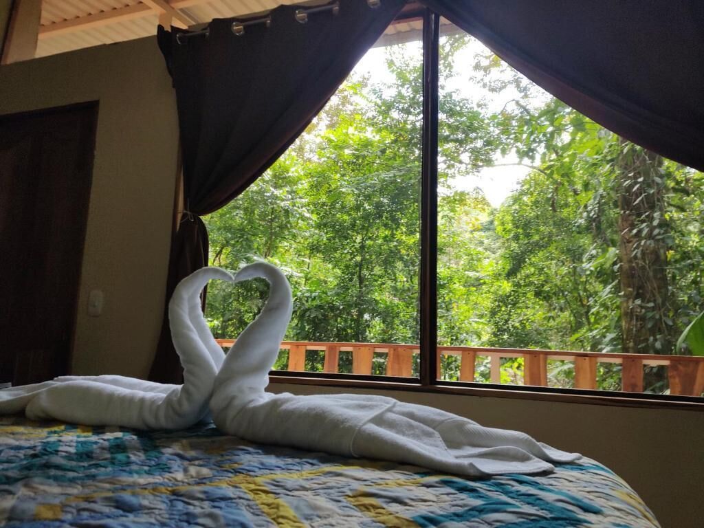 A bed with a quilt and a towel arranged in a heart shape.