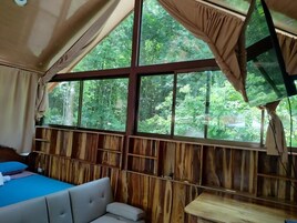 A room with a large window, wooden walls, a bed, and a table.