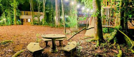 An outdoor area with a round table and benches surrounded by trees and foliage.
