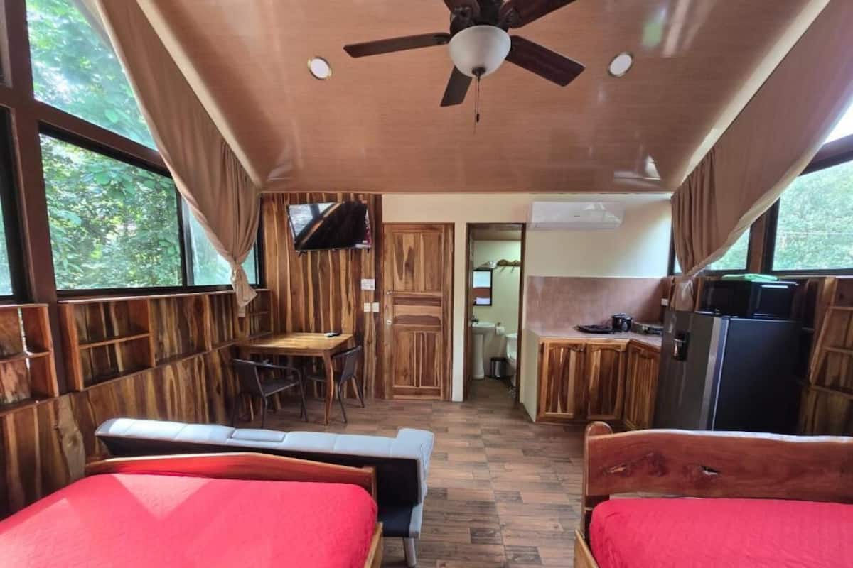 Une chambre de taille modeste, équipée de deux lits, d’un ventilateur de plafond, d’une petite table et d’un coin cuisine.