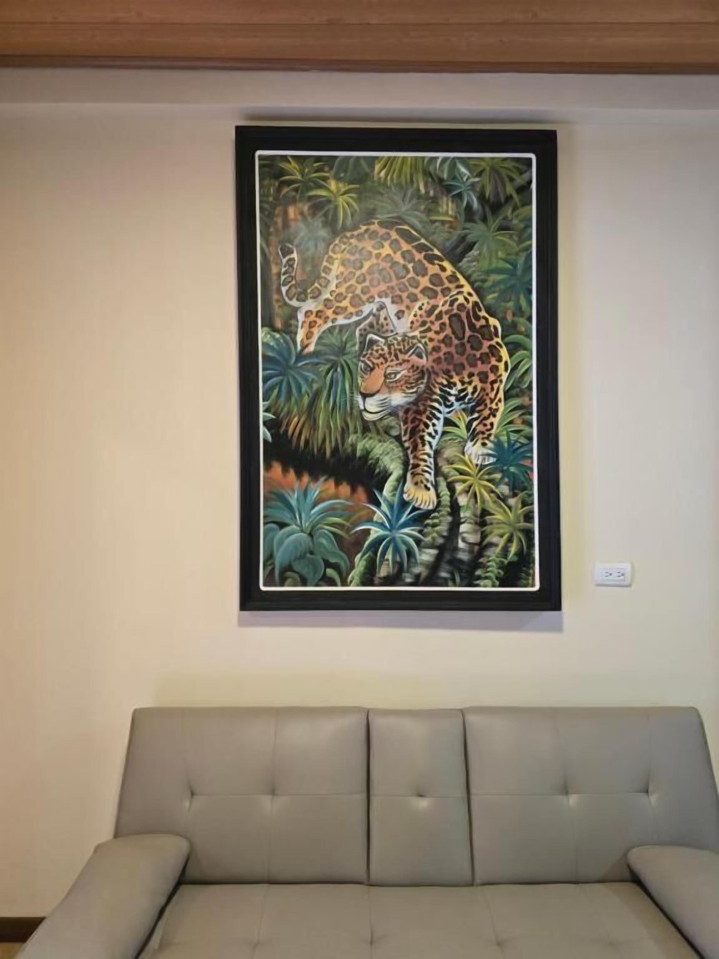 A framed painting of a leopard in a jungle setting on a wall above a grey sofa.