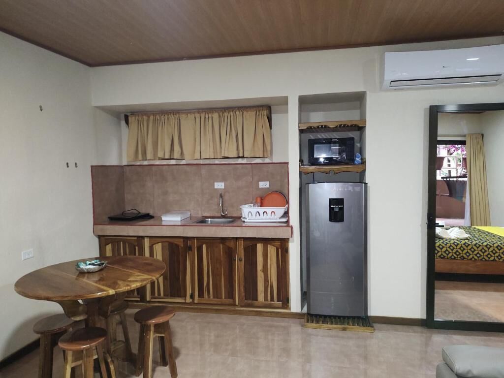 A compact kitchen with a wooden table and stools, a built-in microwave, and a refrigerator.
