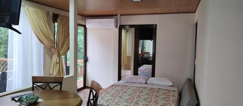 A bedroom with a bed, a chair, a table, and a window with curtains.