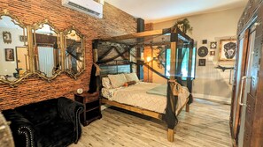 A bedroom with a four-poster bed, a large mirror, and a rustic brick wall.