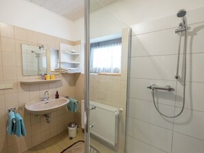 Un baño con lavamanos, espejo, toallero, ducha y ventana.