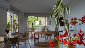 A modern dining area with a wooden table and chairs, a large window with a view of greenery, and a decorative plant in the foreground. - Pousada Mar em Mim (Fernando de Noronha)