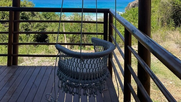 A wooden deck with a hanging chair overlooking a coastal view. - Pousada Mar em Mim (Fernando de Noronha)