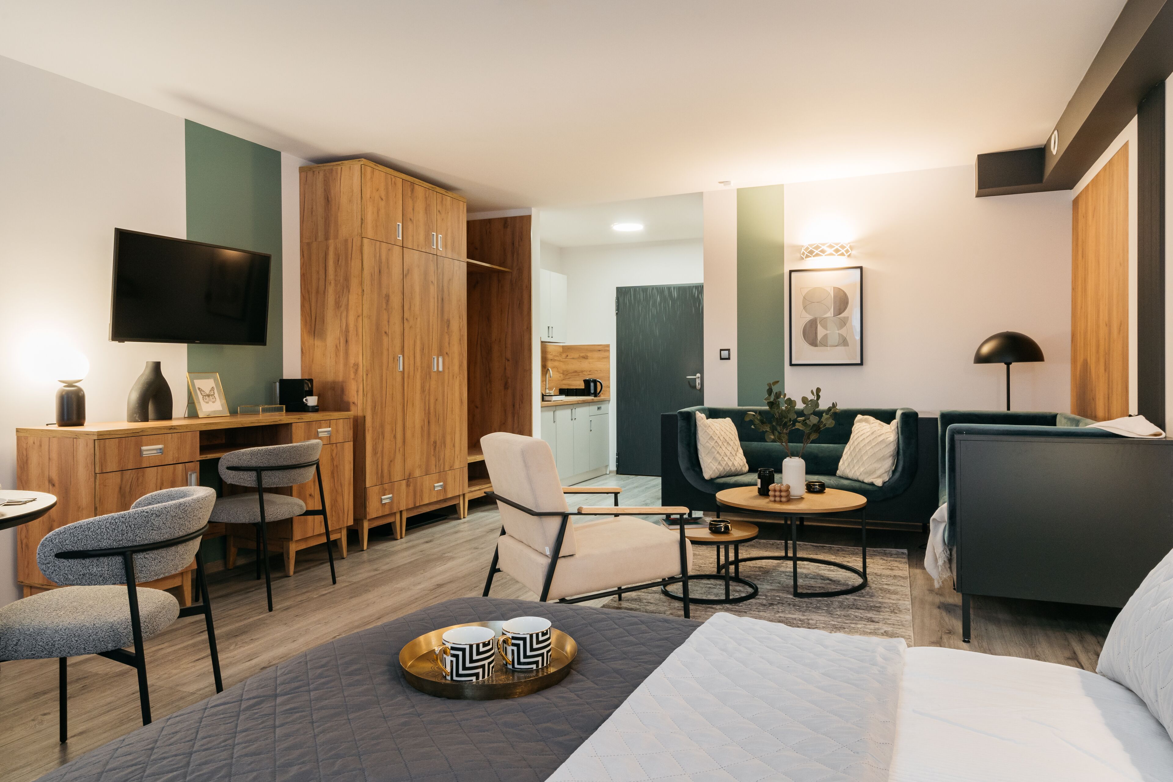 A modern hotel room with a bed, a desk, a TV, and a seating area with a couch and chairs.