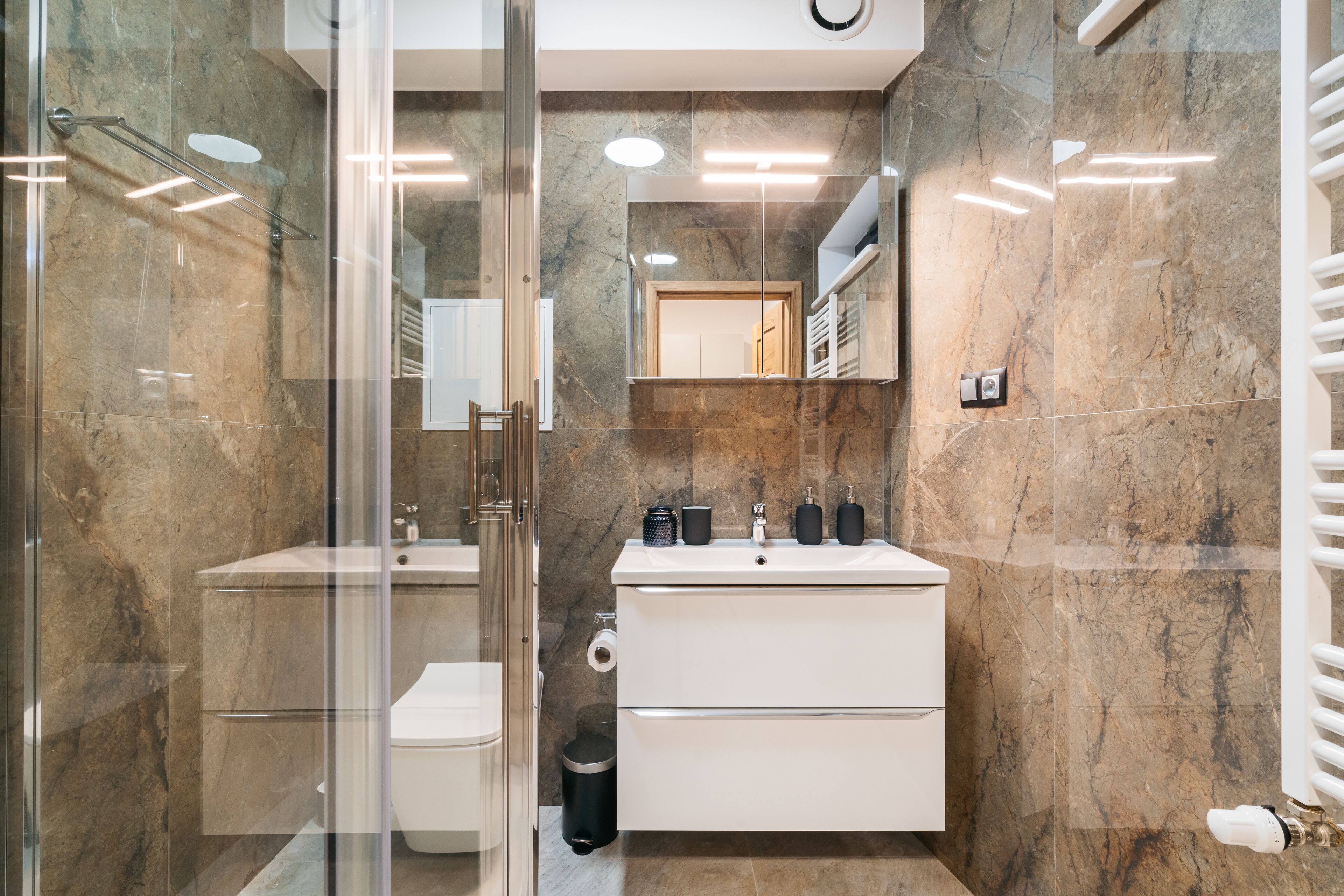 Un baño moderno con cabina de ducha de vidrio, un lavamanos blanco y un espejo grande sobre el mueble.