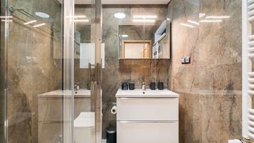 Un baño moderno con cabina de ducha de vidrio, un lavamanos blanco y un espejo grande sobre el mueble.
