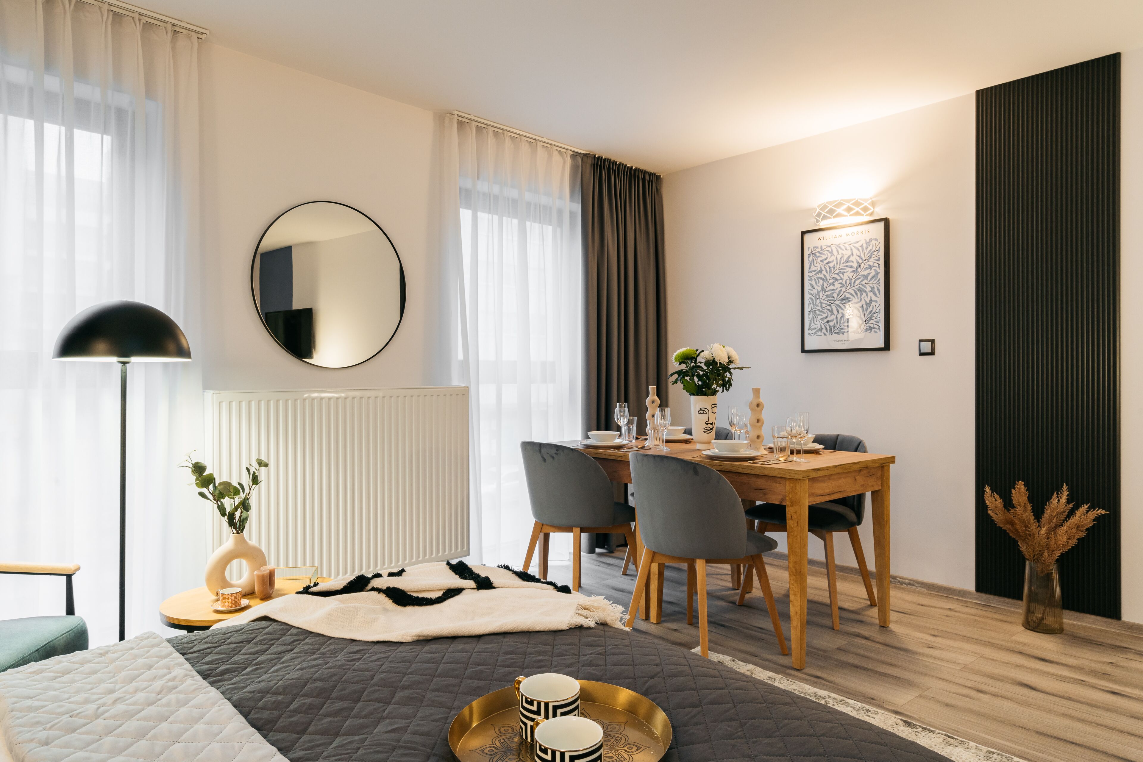 Une chambre d’hôtel moderne équipée d’un lit, d’une table de chevet, d’une lampe et d’un coin repas avec une table dressée pour deux personnes.