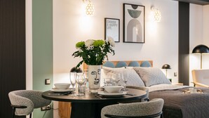 Una habitación de hotel moderna con zona de comedor, una cama con cabecero de madera y una lámpara fijada a la pared.