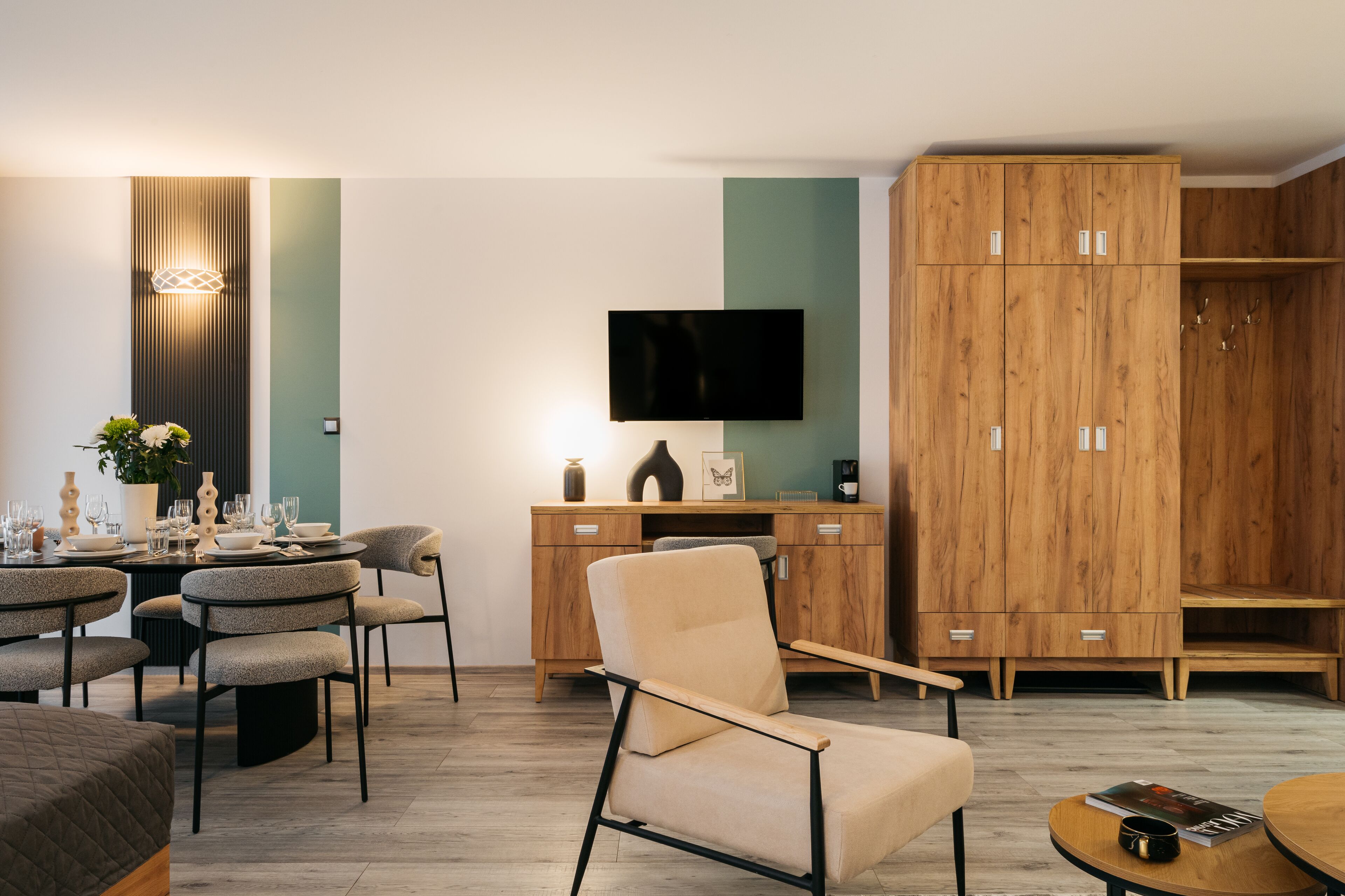 Un soggiorno moderno con zona pranzo, mobili contenitori in legno, televisione a schermo piatto e un'accogliente area salotto.