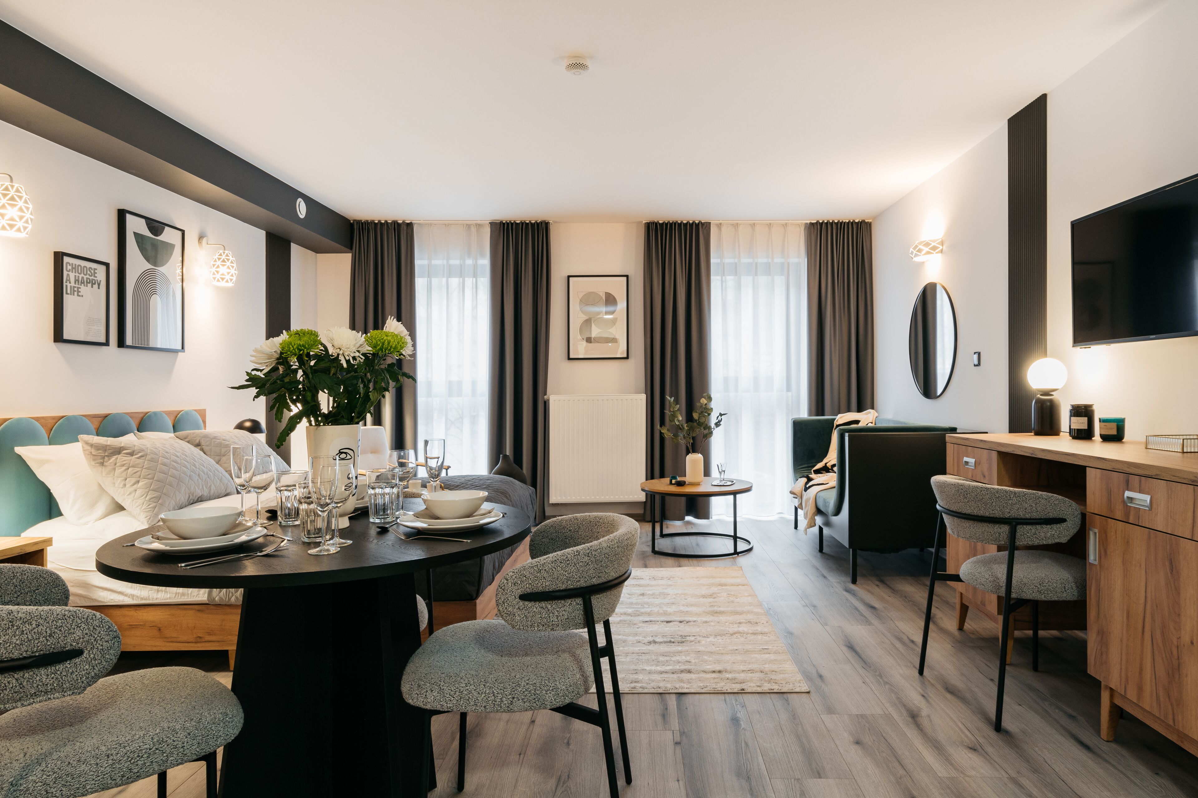 Une chambre d’hôtel moderne dotée d’un coin repas, d’un ensemble de canapés, d’une télévision et d’une grande fenêtre avec des rideaux.