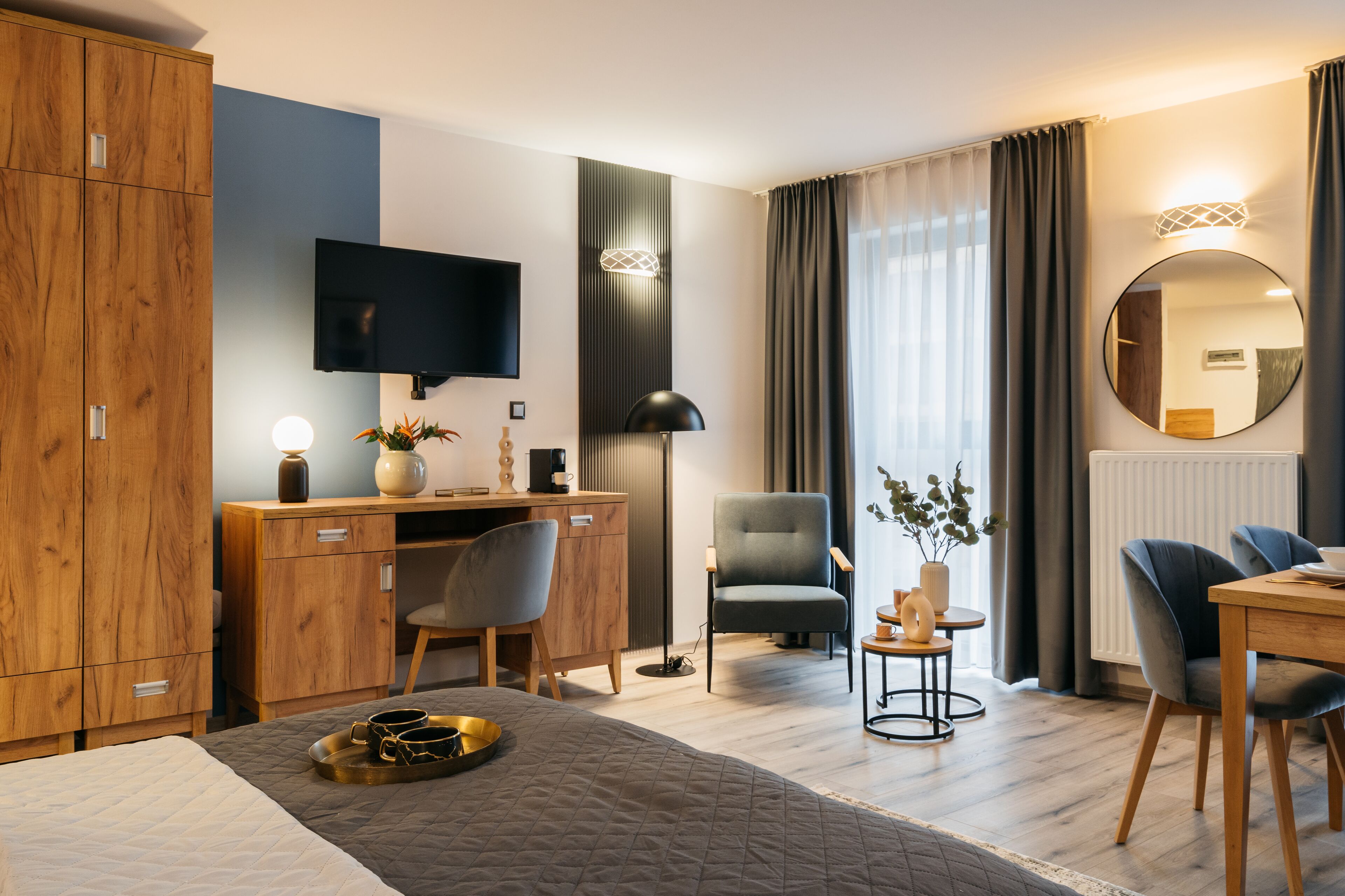 Een moderne hotelkamer met een bed, bureau, stoelen, een televisie en een groot raam met gordijnen.