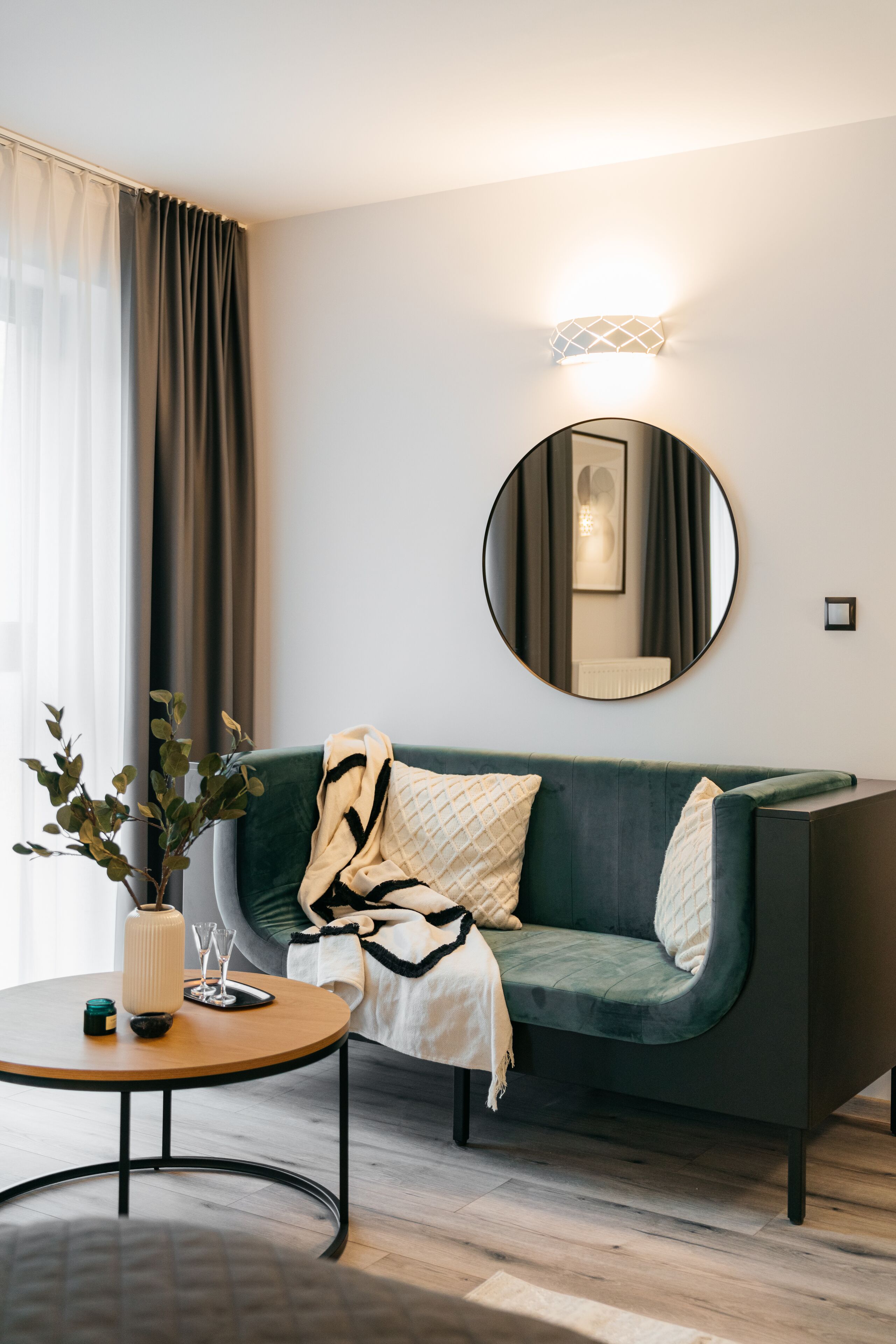 A modern living room with a green sofa, a round mirror, a small round table, and a potted plant.
