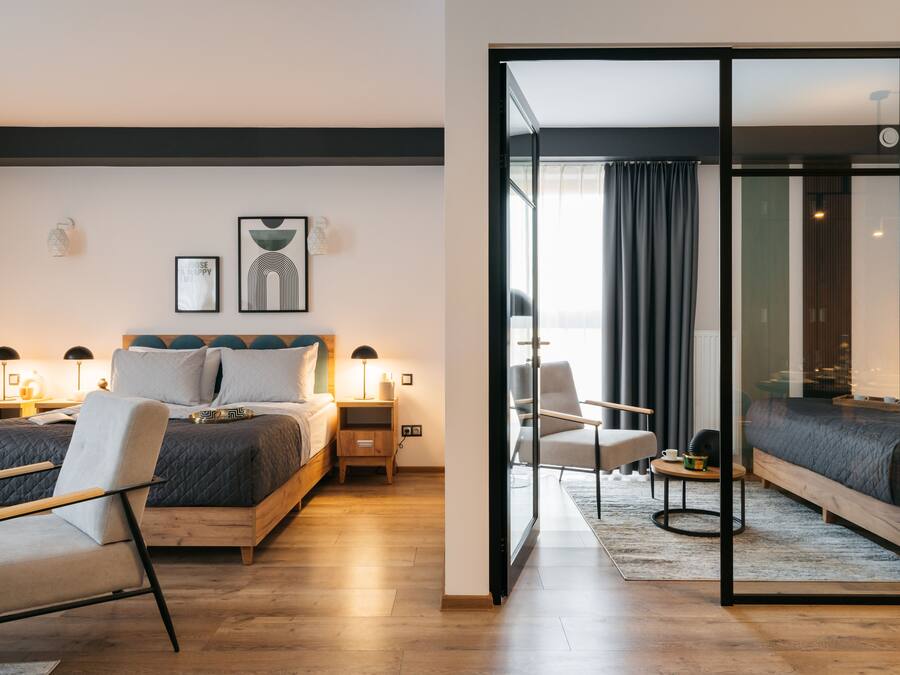A modern hotel room with a large bed, bedside tables, a chair, and a glass partition.
