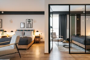A modern hotel room with a large bed, bedside tables, a chair, and a glass partition.