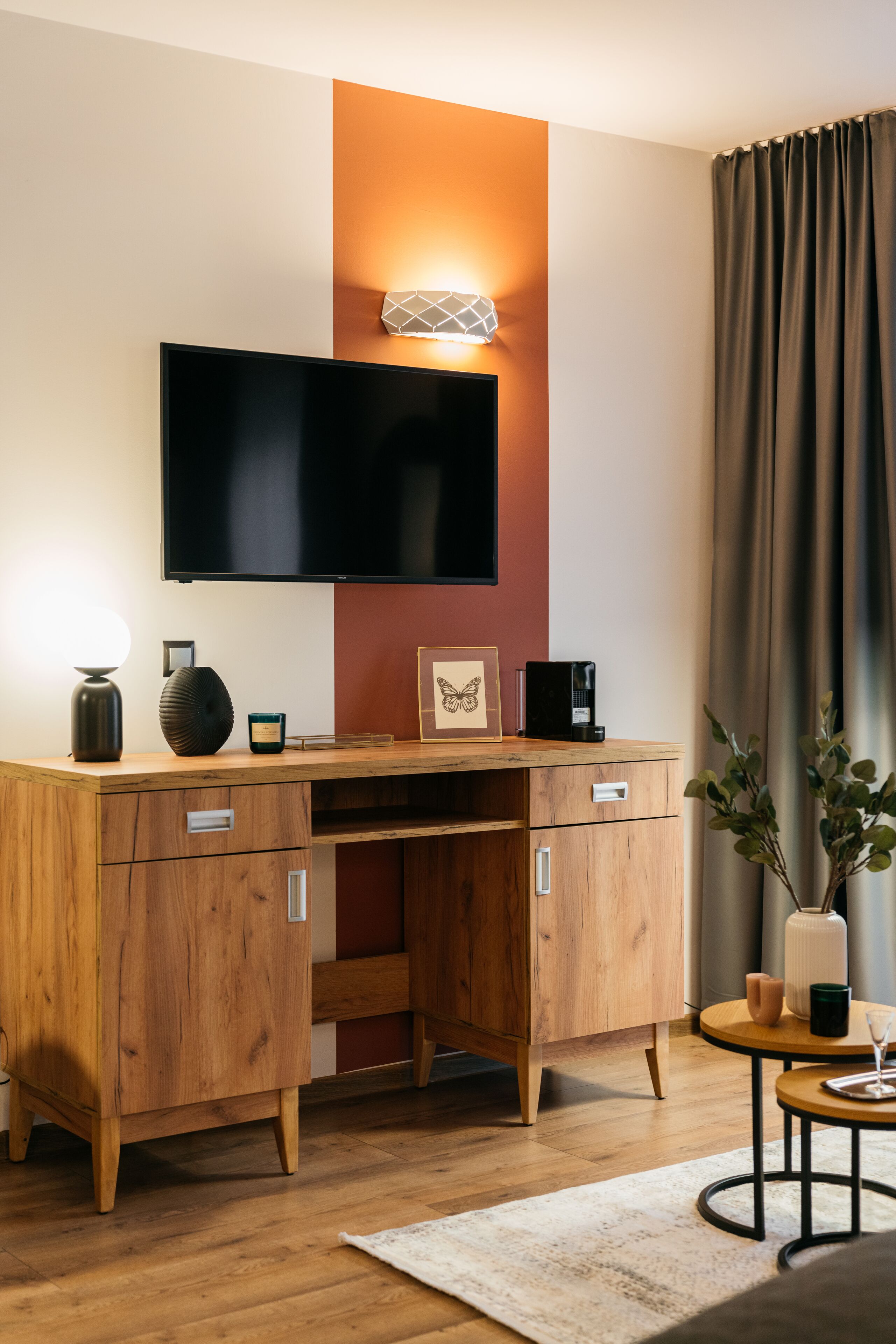 Ein modernes Hotelzimmer mit einem Holztisch, einem Flachbildfernseher, einem Nachttisch mit Lampe und einer Topfpflanze.