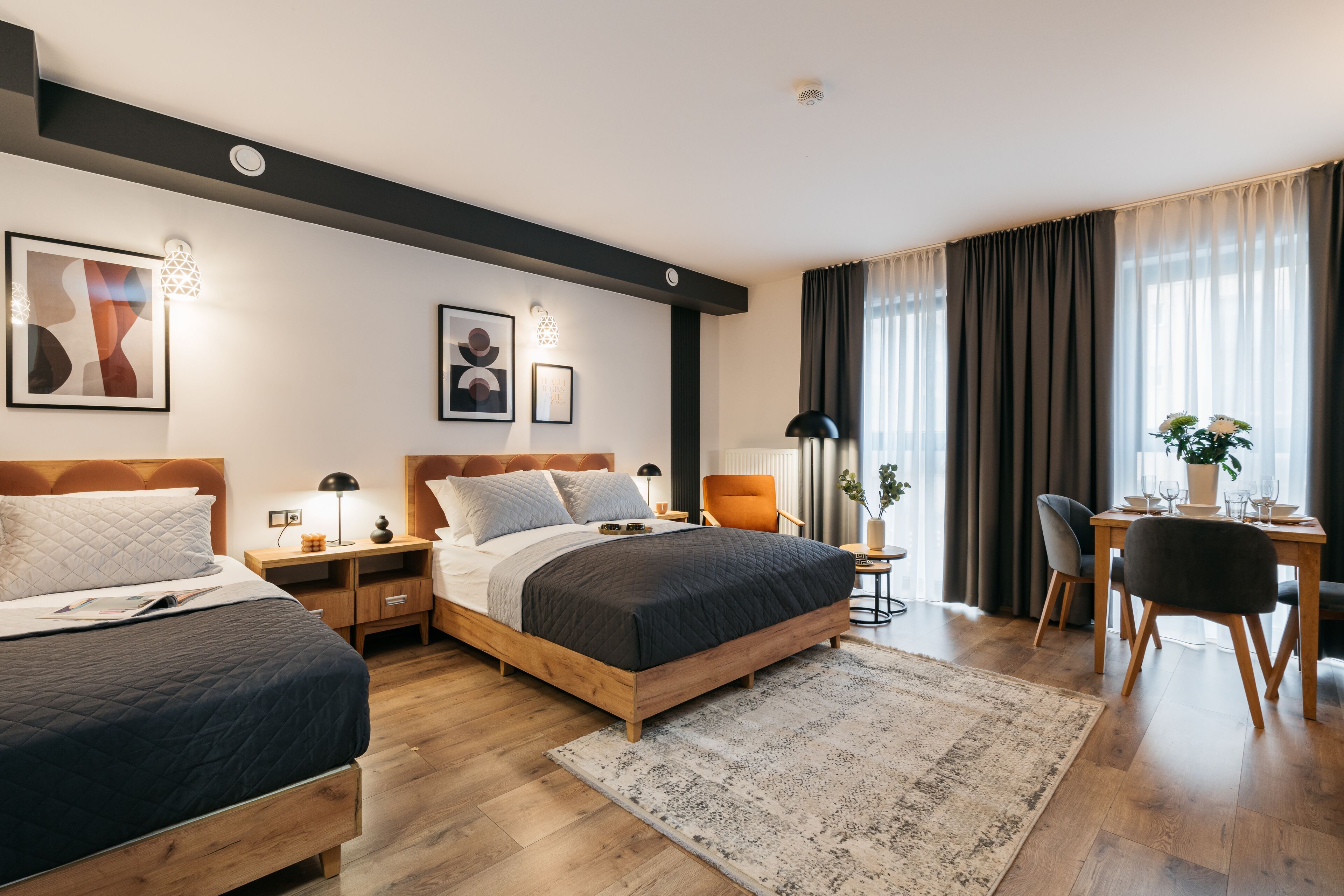 Een moderne hotelkamer met een groot bed, nachtkastjes, een bureau met stoel en een zithoek met gordijnen.