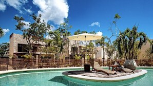 Un espace piscine doté d’une terrasse en bois, de chaises longues et de parasols.