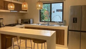 Une cuisine moderne dotée d’un îlot central, d’appareils électroménagers en acier inoxydable et de luminaires suspendus en osier.