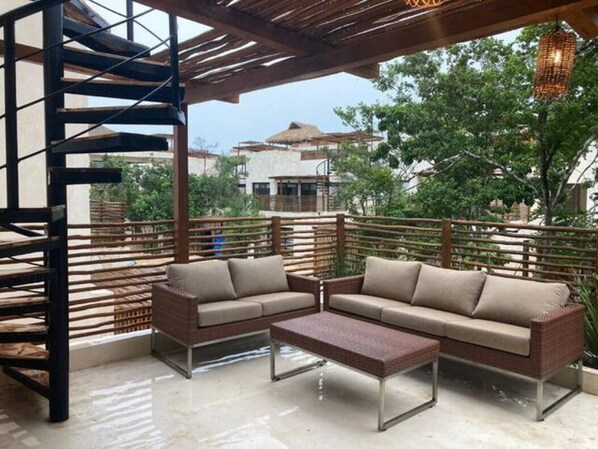 Un área de estar al aire libre con dos sofás y una mesa de centro, rodeada de barandas de madera y una estructura de pérgola.